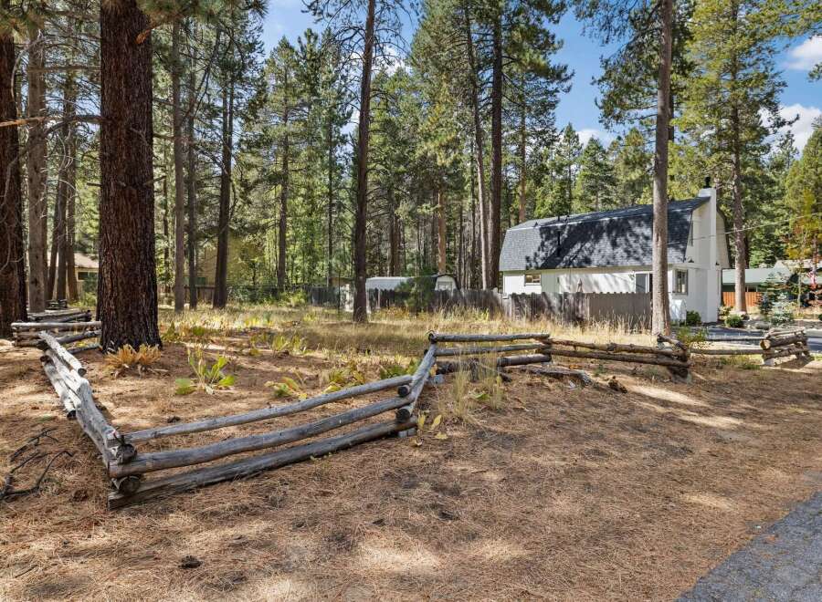 Nestled amidst tall pine trees, this charming property offers a serene retreat with a rustic split-rail fence bordering the grounds.