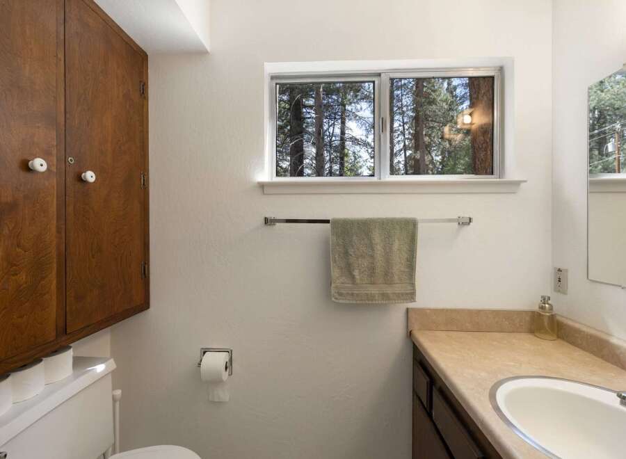 This bathroom features a large wooden cabinet for ample storage, a toilet with extra rolls of toilet paper, and a wall-mounted toilet paper dispenser.