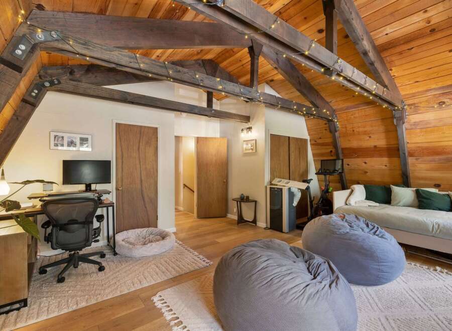 Experience cozy living in this charming attic room, featuring exposed wooden beams and warm wood paneling.