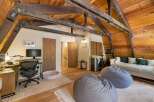 Experience cozy living in this charming attic room, featuring exposed wooden beams and warm wood paneling.