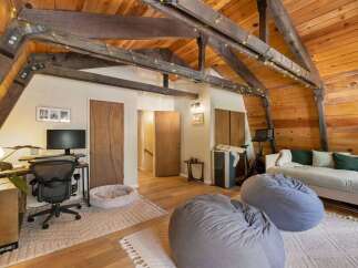 Experience cozy living in this charming attic room, featuring exposed wooden beams and warm wood paneling.