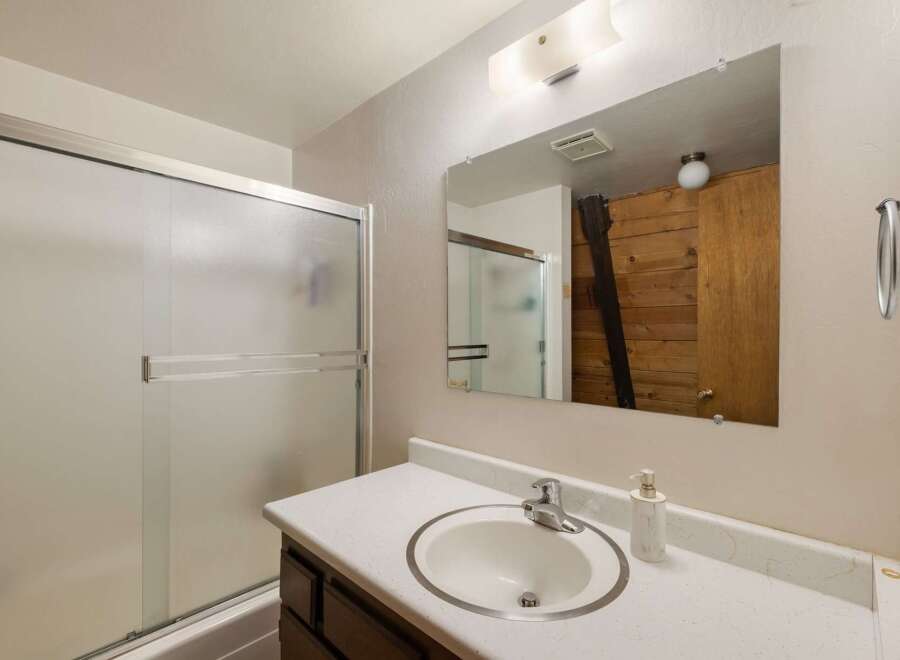 This bathroom features a frosted glass sliding shower door, a white basin sink with a chrome faucet, and a large vanity mirror.