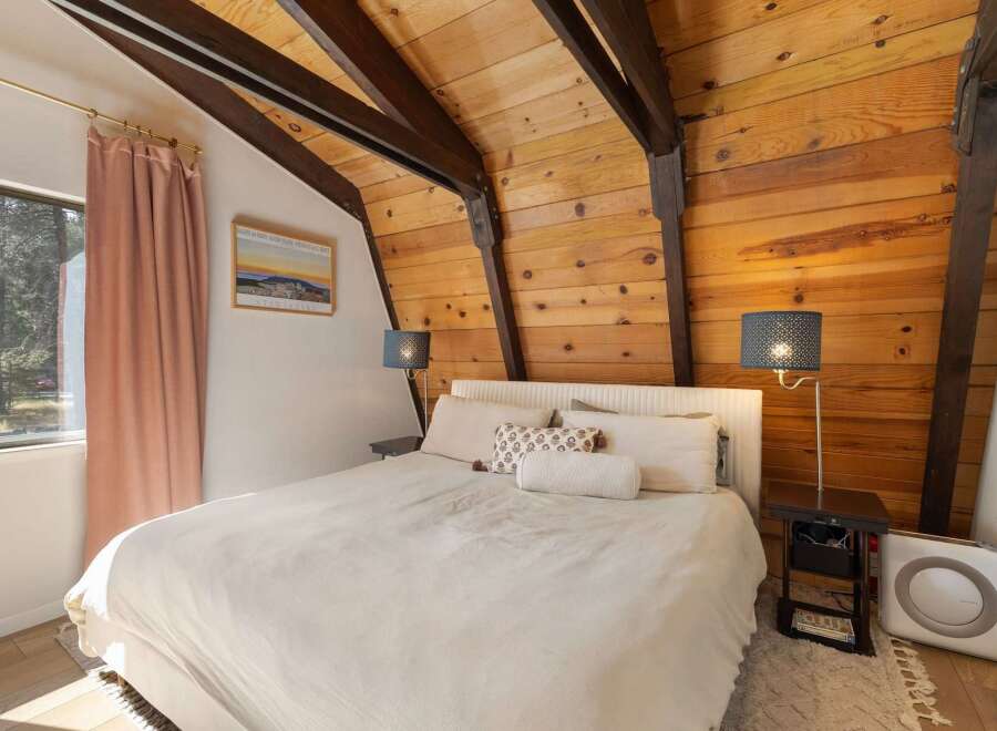Experience cozy mountain living in this charming bedroom featuring a vaulted wood-paneled ceiling with exposed beams.
