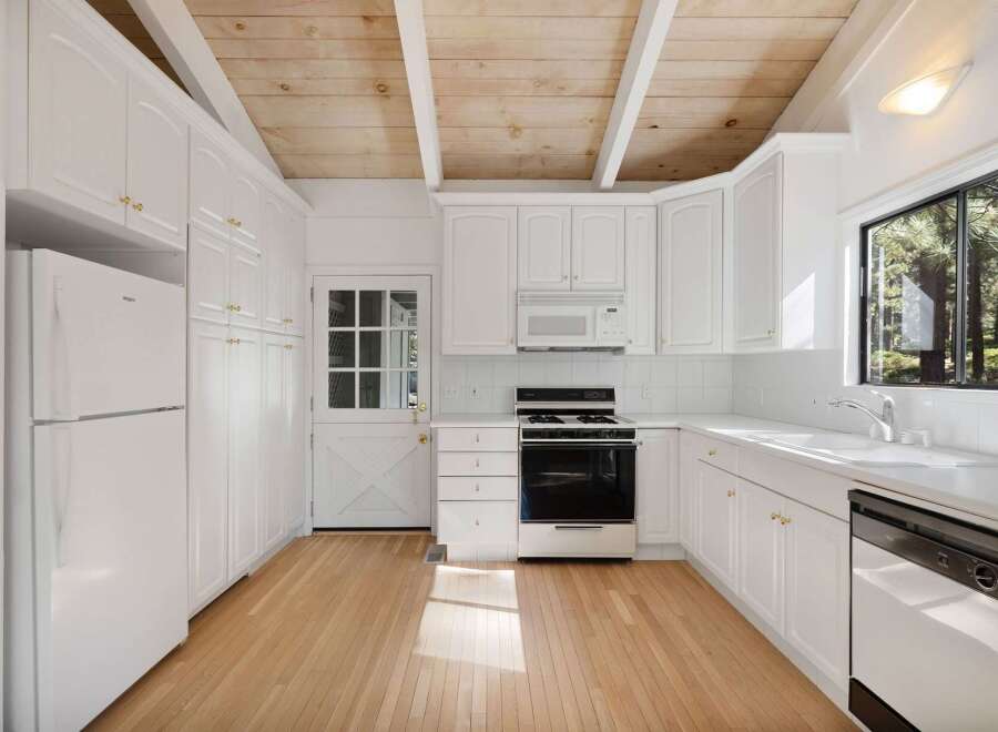 This charming kitchen features white cabinetry with gold hardware, a gas range, and a built-in microwave.