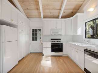 This charming kitchen features white cabinetry with gold hardware, a gas range, and a built-in microwave.