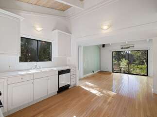 Bright and airy kitchen with white cabinetry and a spacious sink, opening up to a sun-drenched living area with large windows offering serene views of the surrounding greenery.