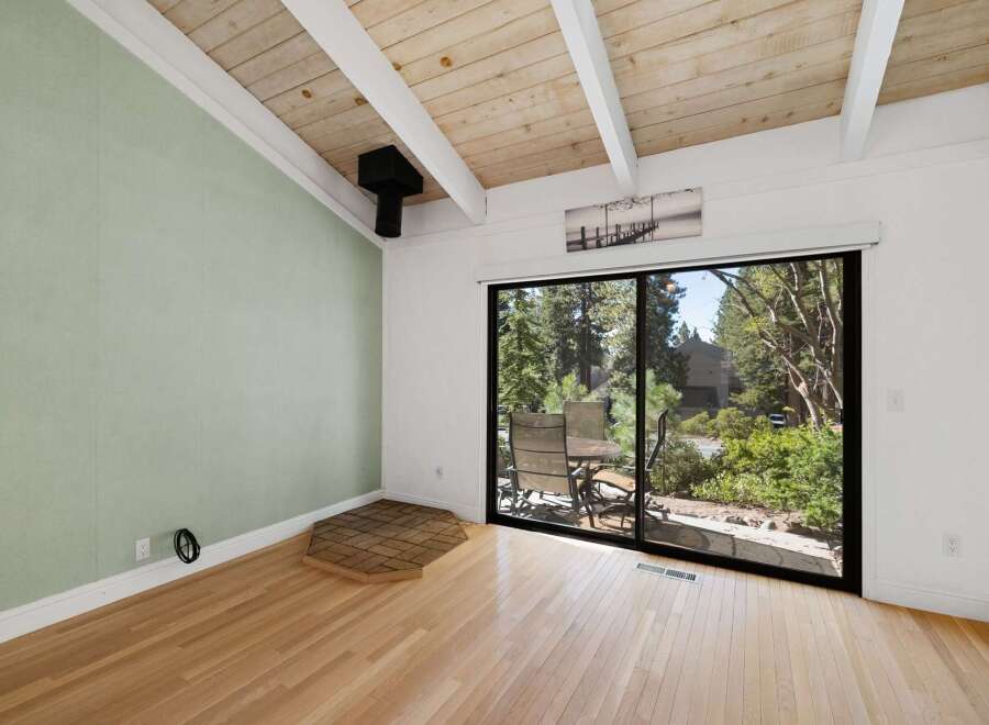 Experience the charm of this inviting room featuring a vaulted wood-beamed ceiling and a large sliding glass door that opens to a serene outdoor space.