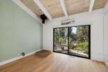 Experience the charm of this inviting room featuring a vaulted wood-beamed ceiling and a large sliding glass door that opens to a serene outdoor space.
