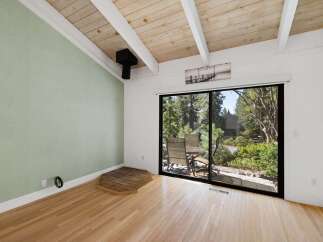 Experience the charm of this inviting room featuring a vaulted wood-beamed ceiling and a large sliding glass door that opens to a serene outdoor space.