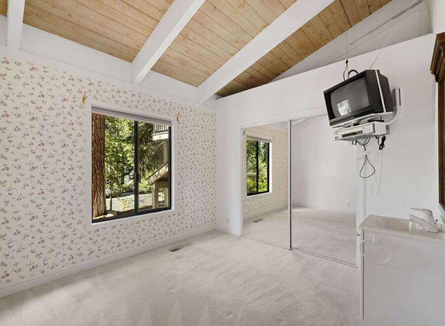 This charming bedroom features a vaulted wood-beamed ceiling and a large window offering serene forest views.