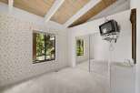 This charming bedroom features a vaulted wood-beamed ceiling and a large window offering serene forest views.