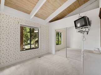 This charming bedroom features a vaulted wood-beamed ceiling and a large window offering serene forest views.