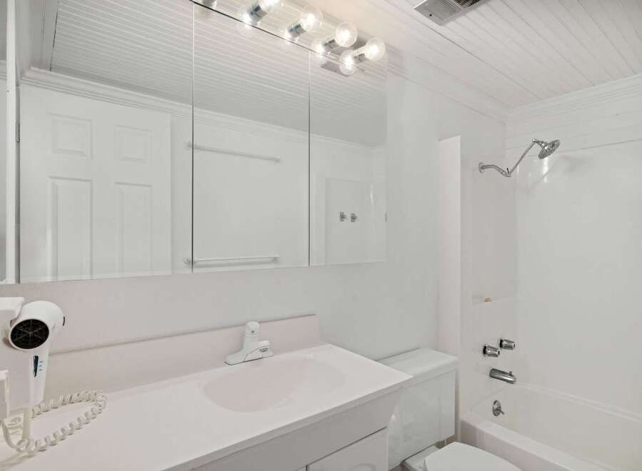 This bright and clean bathroom features a spacious vanity with a large mirror, a wall-mounted hairdryer, and a convenient bathtub/shower combination.