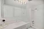 This bright and clean bathroom features a spacious vanity with a large mirror, a wall-mounted hairdryer, and a convenient bathtub/shower combination.