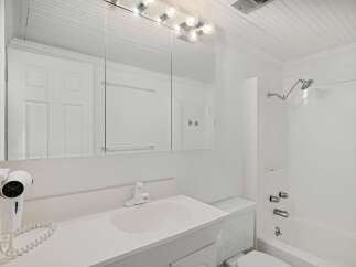 This bright and clean bathroom features a spacious vanity with a large mirror, a wall-mounted hairdryer, and a convenient bathtub/shower combination.