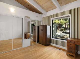 This charming bedroom features a vaulted wood-beamed ceiling and a large window offering scenic views.