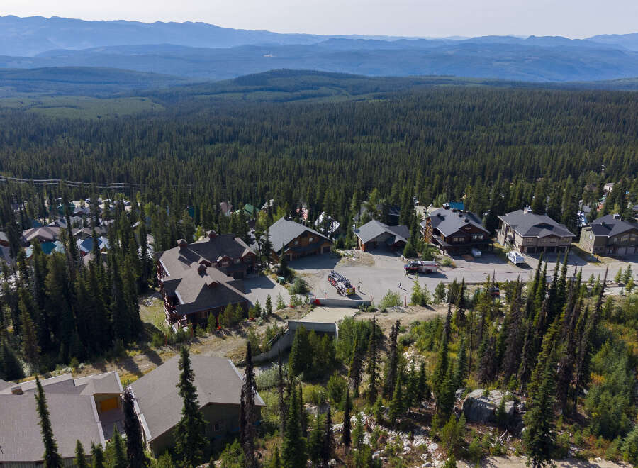 Discover this stunning mountain retreat nestled amidst a dense evergreen forest, offering breathtaking panoramic views of rolling hills and distant blue mountains.