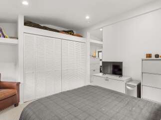 This bedroom features a comfortable brown leather armchair perfect for reading, complemented by a large set of white louvered closet doors.