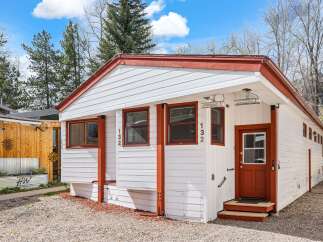 Charming white cottage with red trim, featuring a welcoming red door and multiple windows.