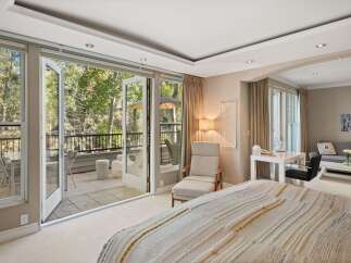 Experience seamless indoor-outdoor living in this luxurious bedroom, featuring expansive glass doors that open onto a private balcony overlooking a serene forest.