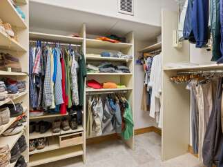 Discover ample storage in this well-organized walk-in closet, featuring extensive shelving for shoes and folded items, alongside a dedicated hanging space for garments.