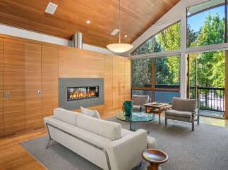 Experience modern living in this stunning living room featuring a sleek gas fireplace and expansive floor-to-ceiling windows that offer breathtaking views of the surrounding greenery.