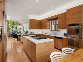 Experience modern luxury in this stunning kitchen featuring sleek, custom wood cabinetry and a spacious island with a built-in gas range.
