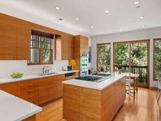 Experience modern living in this stunning kitchen featuring sleek, warm wood cabinetry and a spacious island with a built-in gas range.