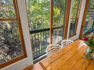 Enjoy breathtaking natural views from this dining area, featuring a rustic wooden table and chairs overlooking a serene stream and lush greenery.