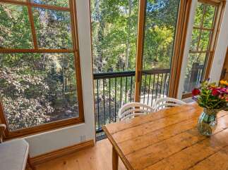 Enjoy a serene dining experience with this charming wooden table, perfectly positioned to offer breathtaking views of a lush forest and a babbling brook through large windows.