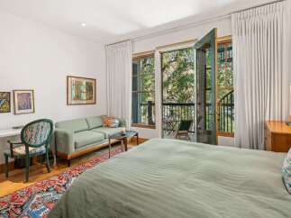 Experience serene living in this charming bedroom, featuring a comfortable bed dressed in soft sage linens and a large window offering lush green views.