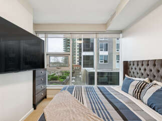 Experience modern urban living in this stylish bedroom featuring a large window with city views and a comfortable king-sized bed.