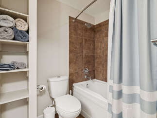 This bathroom features a clean white toilet and a bathtub with brown tiled walls, offering a classic and functional space.