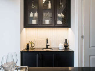 This modern wet bar features sleek black cabinetry and a stylish subway tile backsplash, illuminated by subtle under-cabinet lighting.
