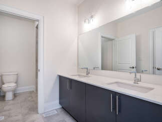 This modern bathroom features a spacious vanity with dual sinks and sleek dark cabinetry, complemented by a large mirror reflecting the elegant interior.