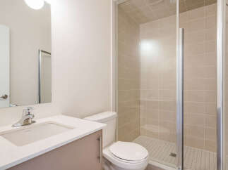 This modern bathroom features a sleek vanity with a white countertop and a chrome faucet, complemented by a spacious walk-in shower with elegant beige tiles.