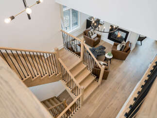Experience modern luxury with this stunning open-concept living space, featuring a grand wooden staircase with black railings that leads to a cozy living area.