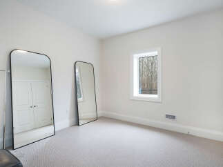 This bright and airy bedroom features a large window offering a view of the surrounding trees.