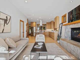 Experience modern living in this beautifully renovated open-concept space, featuring a sleek kitchen with natural wood cabinetry and a spacious living area centered around a cozy stone fireplace.