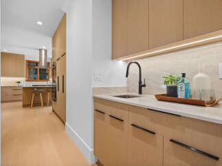 Experience modern luxury in this stunning kitchen featuring sleek, light wood cabinetry and a sophisticated wet bar area.