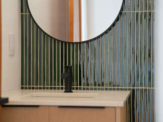 This modern bathroom features a sleek vanity with a light-colored countertop and a black faucet, complemented by a striking vertical tile backsplash in shades of deep green and cream.