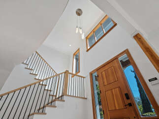 Experience modern living in this stunning entryway featuring a grand wooden door and a soaring ceiling with a contemporary chandelier.