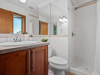 This modern bathroom features a sleek vanity with a granite countertop and a white undermount sink, complemented by a large mirrored wall.