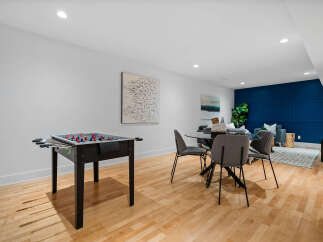 This modern basement living area features a foosball table for entertainment and a stylish dining set with a glass-top table and gray chairs.