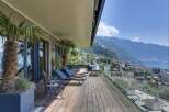 Experience luxurious outdoor living on this expansive wooden deck, complete with comfortable lounge chairs and stunning panoramic views of the lake and mountains.