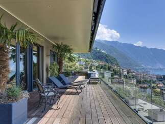 Experience luxurious outdoor living on this expansive wooden deck, complete with comfortable lounge chairs and stunning panoramic views of the lake and mountains.
