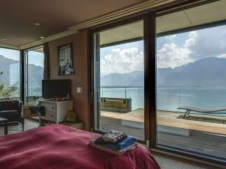 Experience breathtaking lake and mountain views from this luxurious bedroom, featuring expansive sliding glass doors that open onto a private deck.