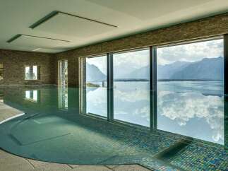 Experience luxury living with this stunning indoor swimming pool, featuring breathtaking panoramic views of majestic mountains and a serene lake.