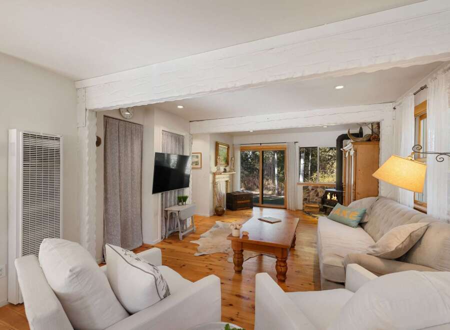 Experience cozy living in this charming living room, featuring a wood-burning stove and a large picture window offering serene forest views.