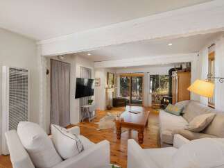 Experience cozy living in this charming living room, featuring a wood-burning stove and a large picture window offering serene forest views.